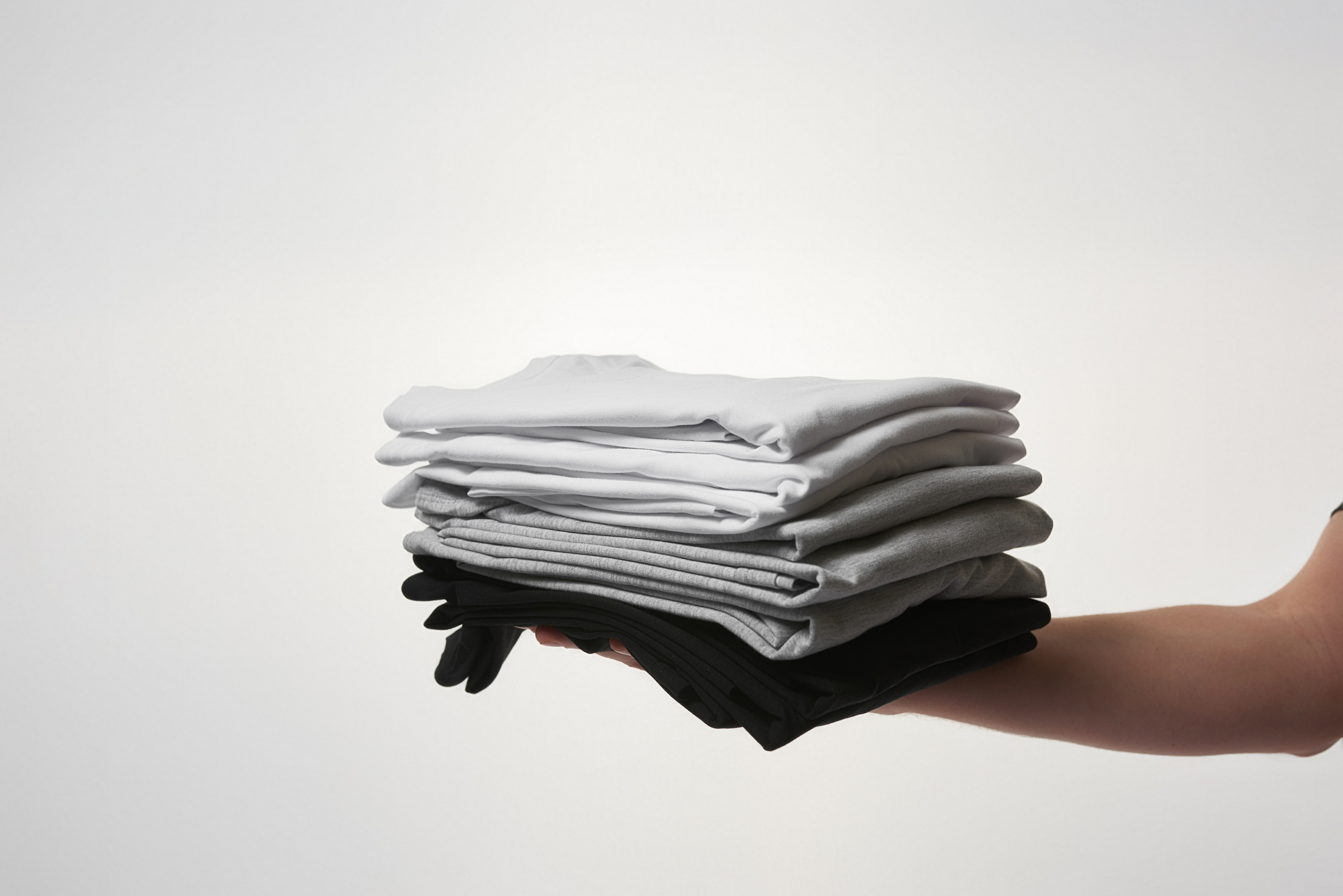 Male hand holding stock of basic T-shirts against grey background